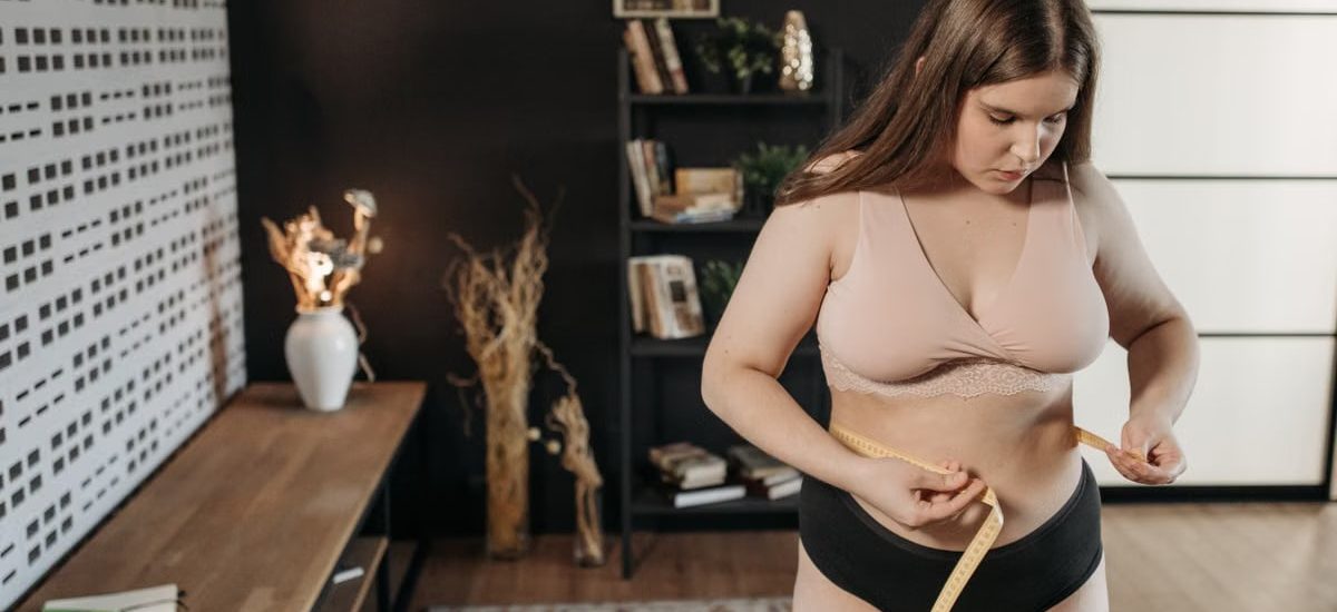 A plus size woman measures her waist indoors, focusing on body positivity and self-care.