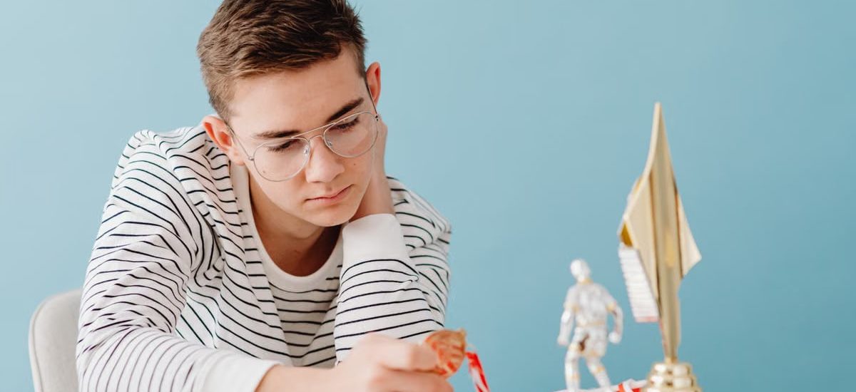 Young man with eyeglasses examines his medals and trophies, reflecting success.