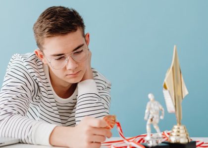 Young man with eyeglasses examines his medals and trophies, reflecting success.